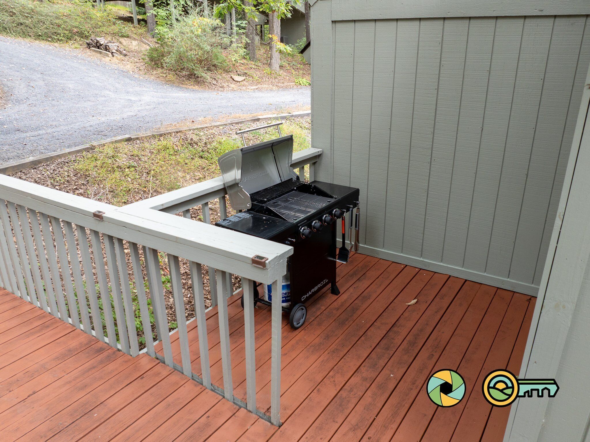 A barbecue grill on a wooden deck with a white railing and a gray building in the background.
