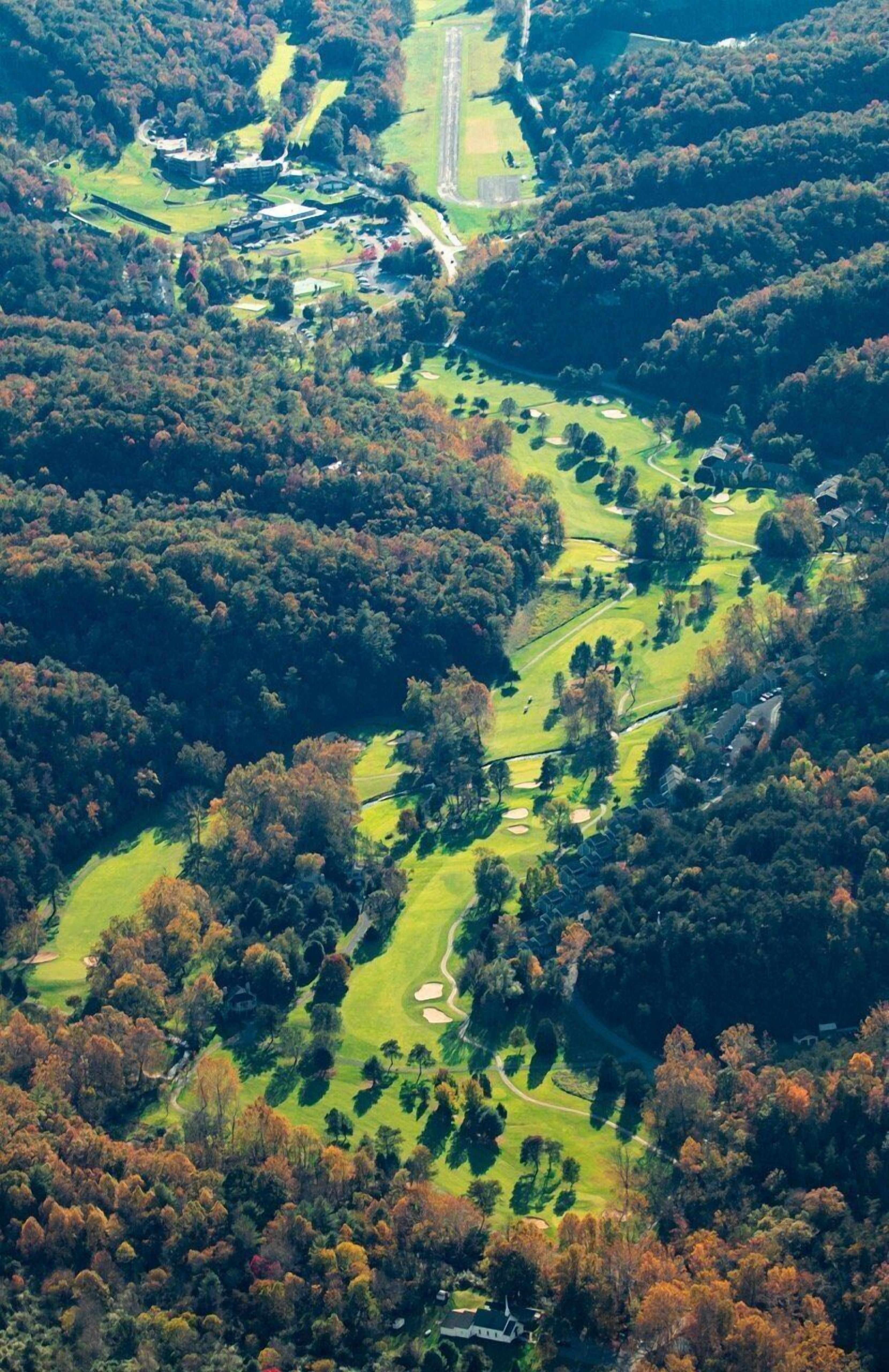 Eine Vogelperspektive auf einen Golfplatz mit mehreren Bahnen, umgeben von dichtem Wald.