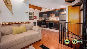 A cozy living room with a sofa and a staircase leading to a kitchen area. - Treehouse Mountain Stay - unique cozy quiet! (Basye)