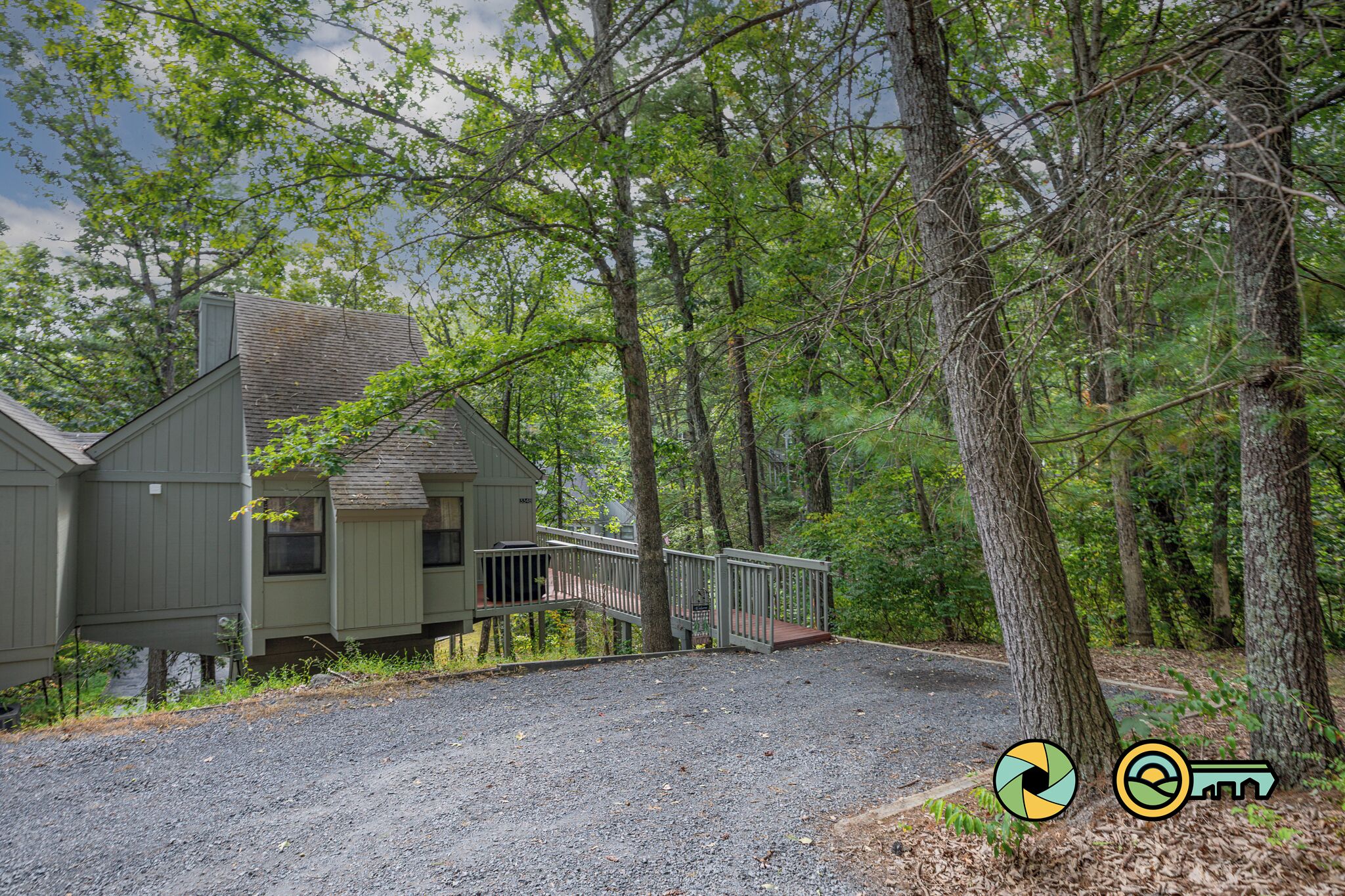 A cabin with a gravel driveway and a wooden deck, surrounded by dense forest.
