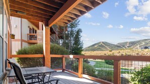 A wooden deck with a table and chairs, overlooking a mountainous landscape with a golf course.