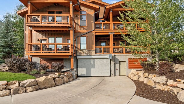 A multi-story wooden building with balconies, a garage, and a landscaped driveway.