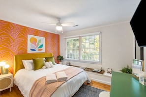 A bedroom with a bed, a ceiling fan, a window with blinds, and a wall with a leaf pattern. - 5BR Group House | Fire Pit, Movie Deck & Fun Games (Charleston)
