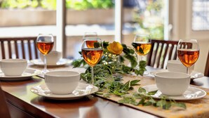 Une table à manger est dressée avec des bols blancs et des verres contenant un liquide ambré, probablement du thé, le tout entouré de verdure et d’une fleur jaune.