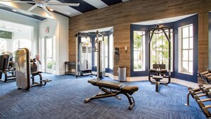 Une salle de sport équipée de matériel d’exercice, dotée de grandes fenêtres et d’un ventilateur de plafond.