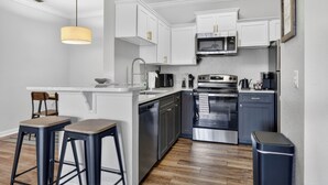 Une cuisine moderne avec des meubles blancs, des appareils en acier inoxydable et un coin bar avec des tabourets.