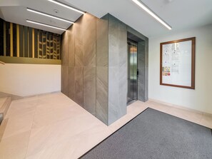 Um interior moderno com escada, elevador embutido na parede e um mural de avisos.