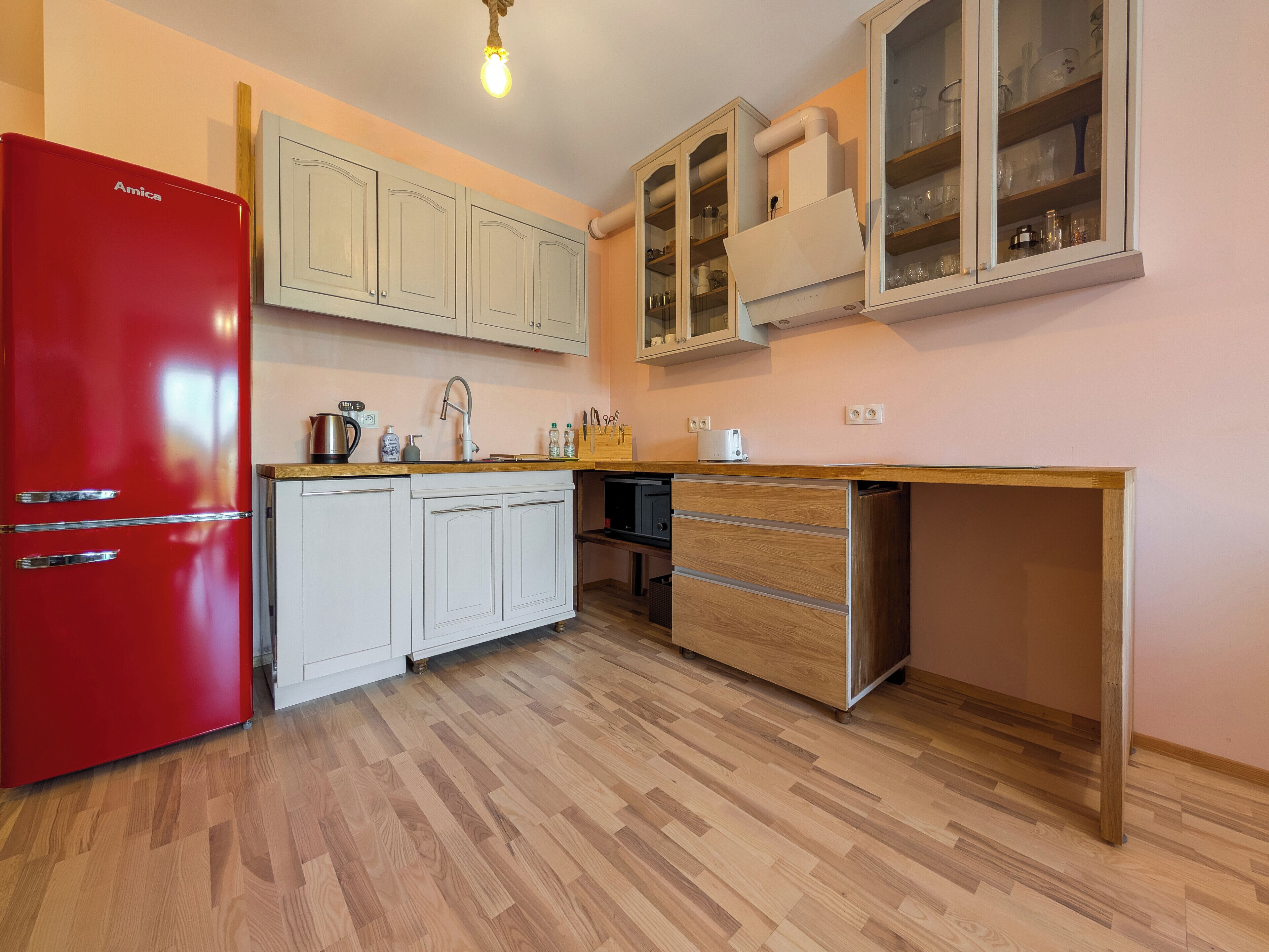 Une cuisine de taille réduite avec un réfrigérateur rouge, des armoires blanches et un plan de travail en bois.
