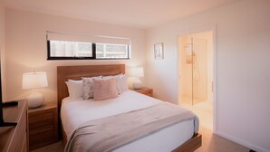 Une chambre d’hôtel avec un grand lit, deux tables de chevet avec des lampes, une fenêtre donnant sur un beau paysage et un espace douche.