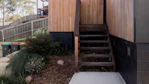 Un bâtiment moderne doté d’une façade en bois, d’un chemin en béton menant à un escalier et d’une clôture en métal en arrière-plan.