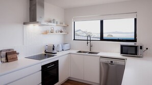 Une cuisine moderne avec des meubles blancs, un lave-vaisselle, un four à micro-ondes, un grille-pain et une fenêtre donnant sur un pont et l’eau.