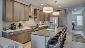 A modern kitchen with stainless steel appliances, wooden cabinets, and a central island with bar stools. - Rooftop retreat with views of Belmont-Near The Gulch! (Nashville)