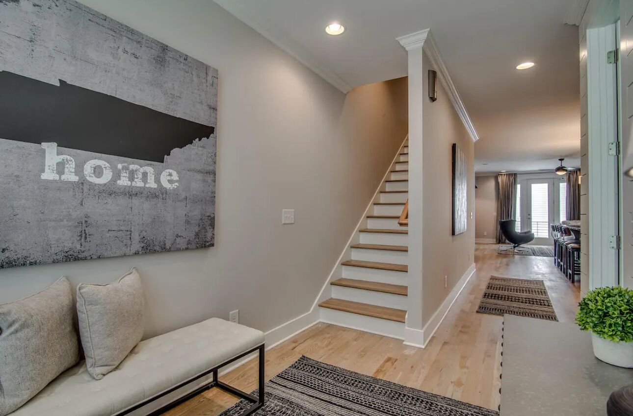 A modern interior with a staircase, a sofa with cushions, and a wall with the word "home" on it.