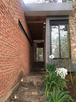 Un edificio de ladrillo con un pórtico cubierto, escalones de piedra y una ventana con vistas a árboles.