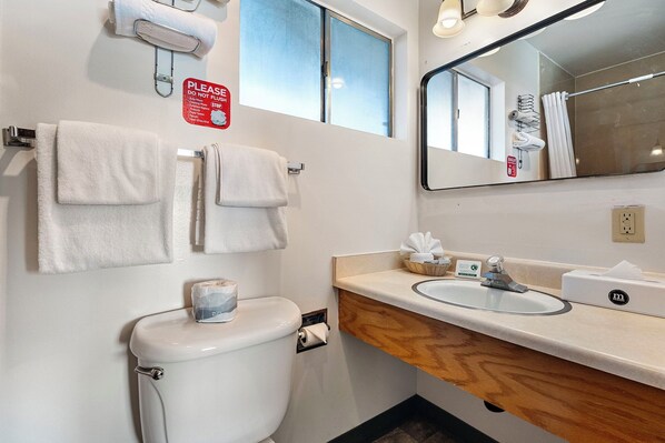 A bathroom with a toilet, two towels hanging on a rack, a sink with a mirror, and a window above the toilet.