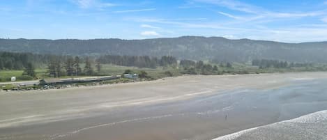 Un paisaje costero con una playa, colinas boscosas y cielo despejado.
