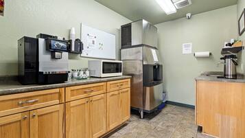 A kitchen with a coffee machine, microwave, refrigerator, and wooden cabinets.