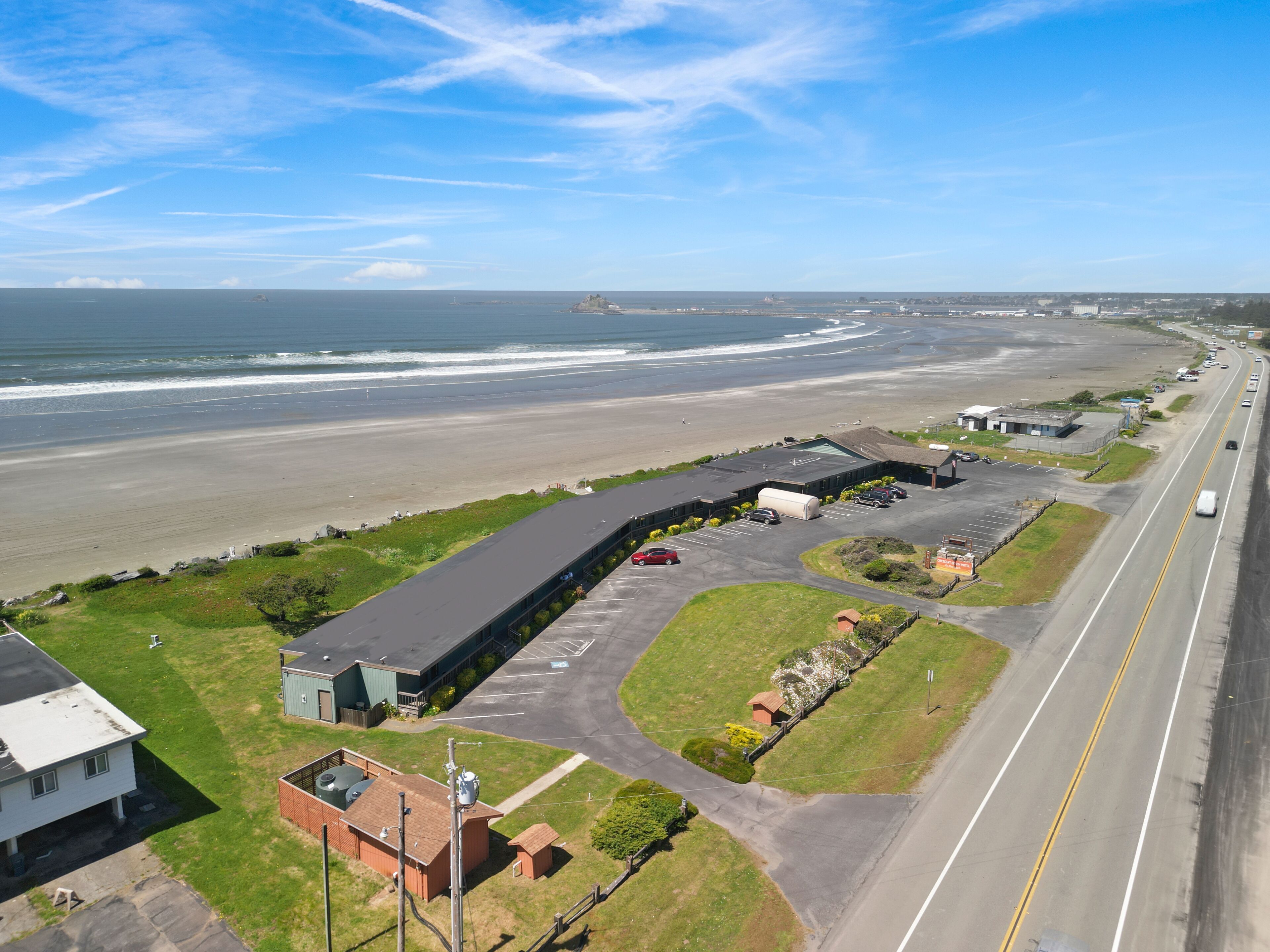 Vista aérea de una propiedad costera con un edificio grande, estacionamiento y una playa al fondo.