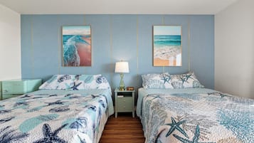 Quarto com duas camas, cada uma com colcha decorada com tema de estrela-do-mar, mesa de cabeceira com abajur e duas fotos emolduradas de praias na parede.