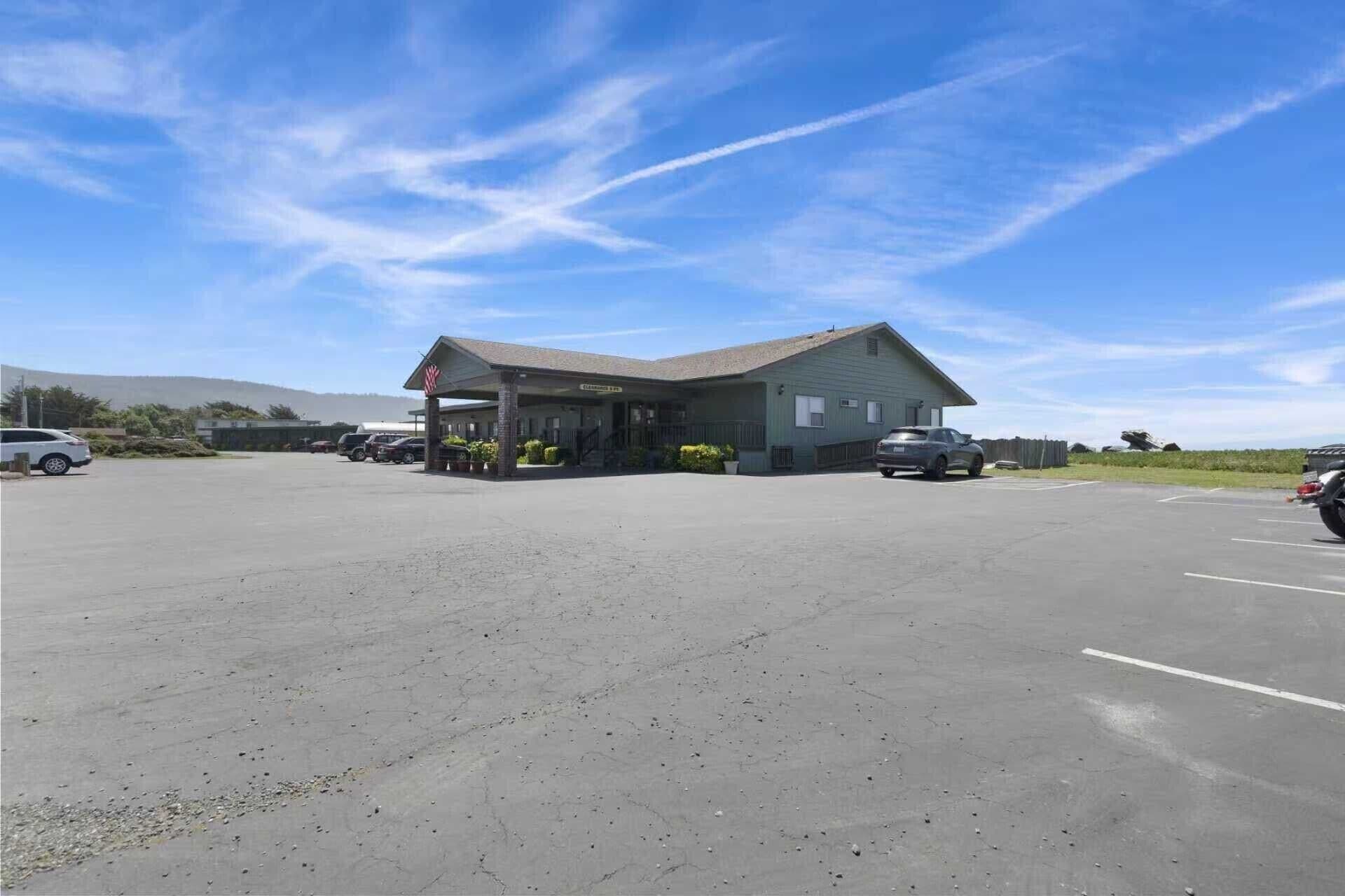Ein Gebäude mit überdachter Einfahrt, Parkplatz und blauem Himmel.