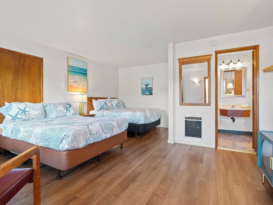 A bedroom with two beds, a wooden wardrobe, a desk, and a mirror.