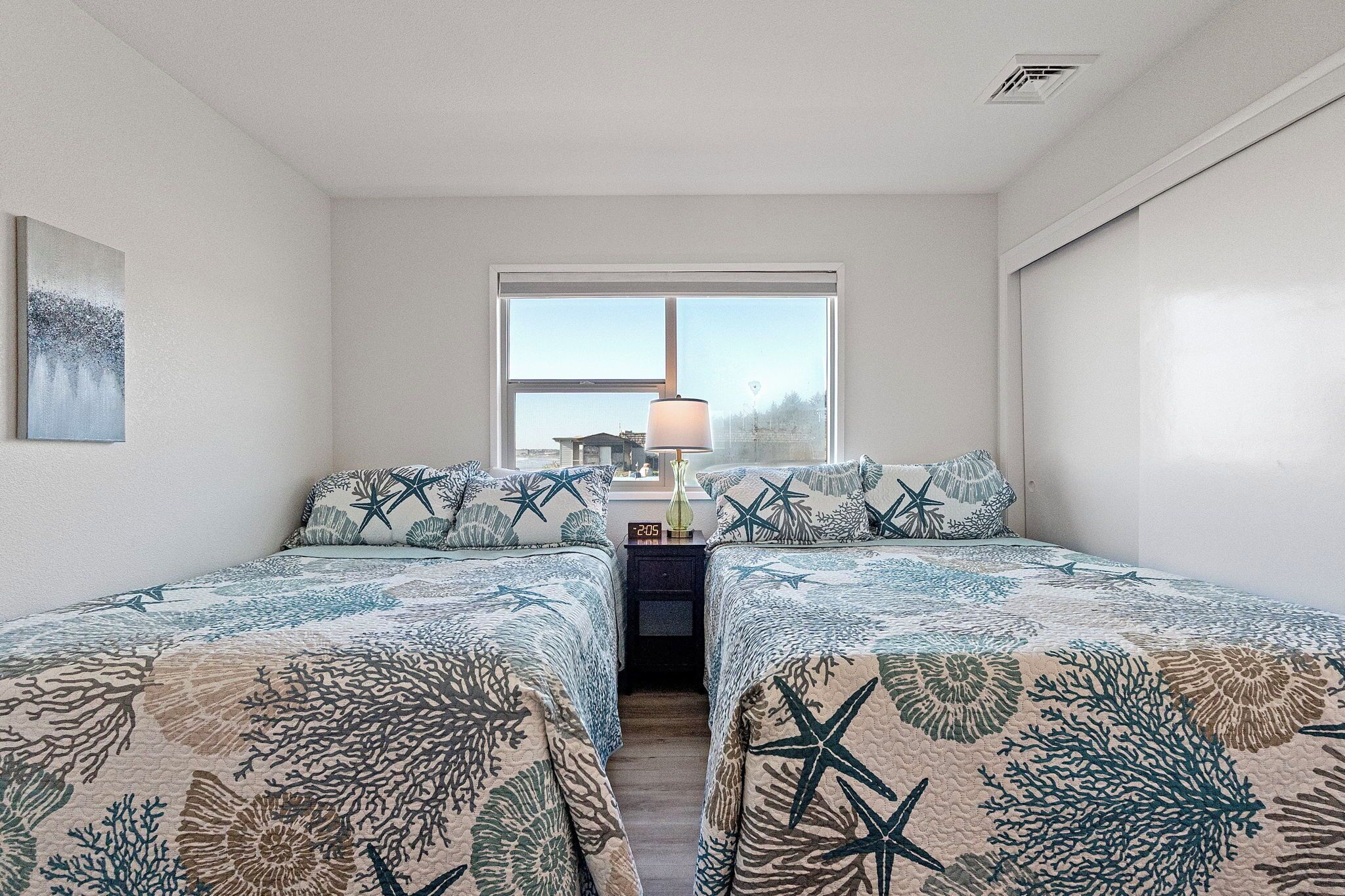 Quarto com duas camas, mesa de cabeceira, abajur e janela com vista.
