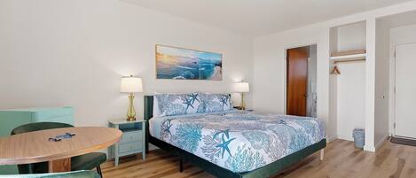 A bedroom with a bed, a desk, and a chair. There is a painting on the wall and a door to the right.