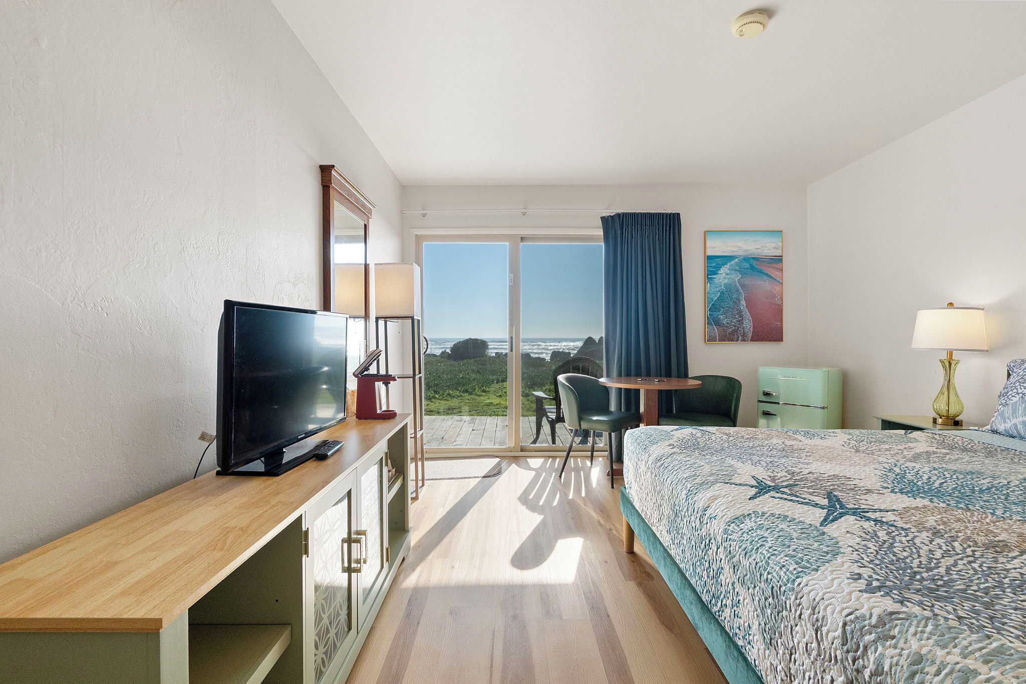Habitación de hotel con una cama grande, un escritorio con televisor, una silla, una mesita y vistas al exterior.