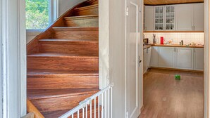 Un escalier en bois mène à une cuisine dotée de meubles blancs et d’une fenêtre.