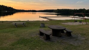 Un parc au bord du lac, équipé de tables de pique-nique, d’une aire de jeux avec des balançoires et d’une jetée qui s’avance dans l’eau.