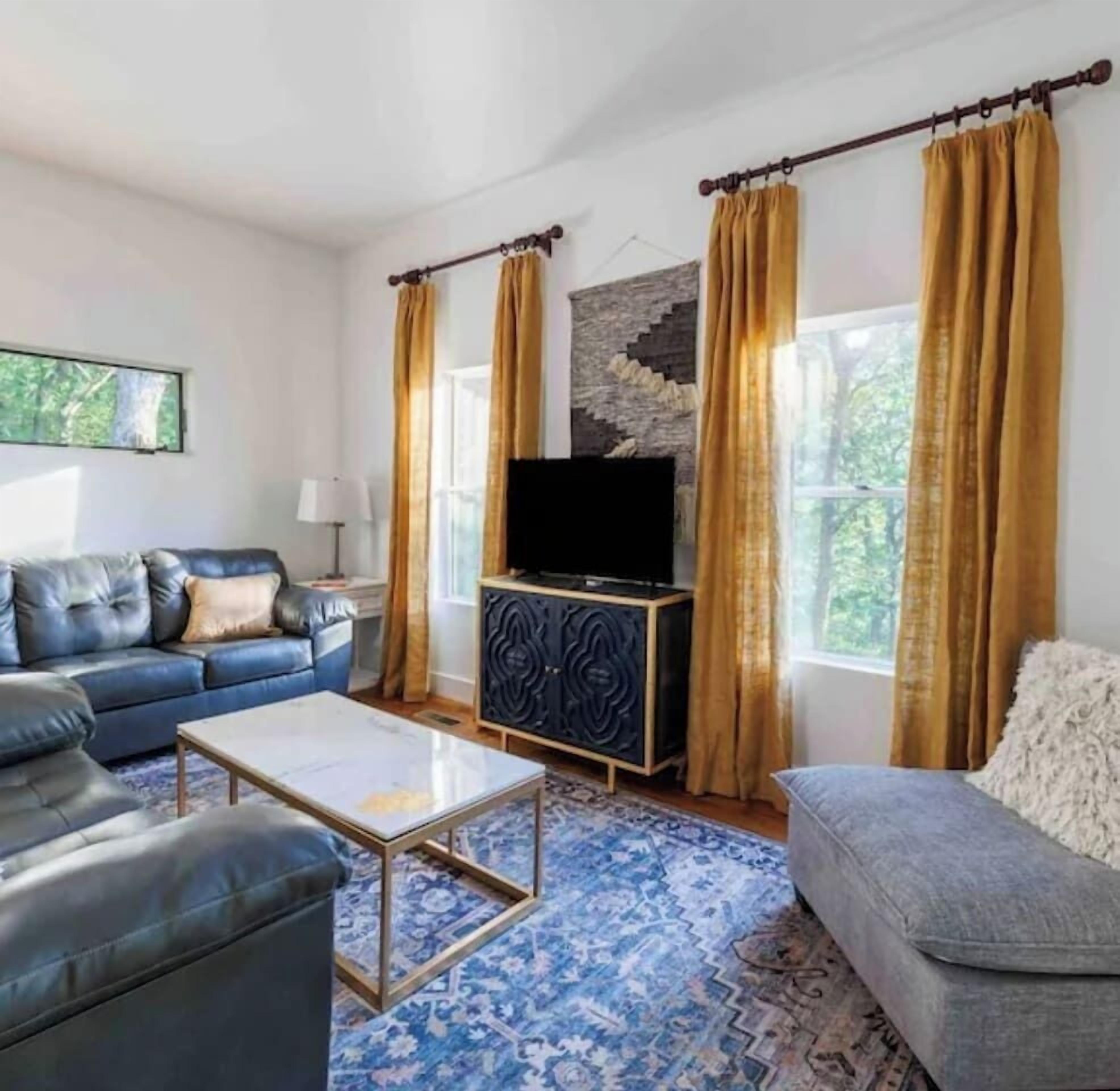 Ein Wohnzimmer mit blauem Sofa, grauem Sofa, Couchtisch, Fernseher auf einem schwarzen Schrank und einem gemusterten Teppich.