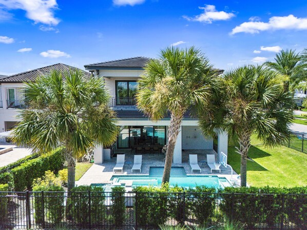 A modern two-story house with a swimming pool, surrounded by palm trees and a well-maintained lawn.