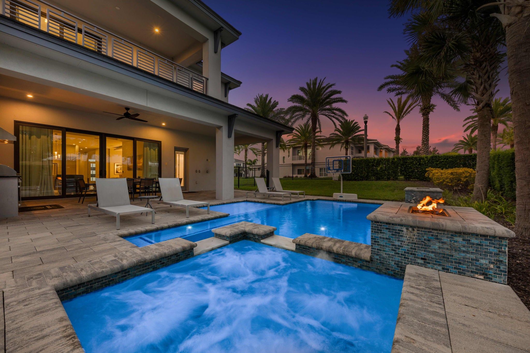 A swimming pool with a hot tub, lounge chairs, and a fire feature.