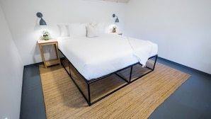 A bedroom with a bed, two bedside tables, two wall-mounted lamps, and a small potted plant on one of the tables.