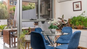 Une terrasse moderne avec une table en verre, entourée de chaises bleues, de plantes en pot et d’un banc en bois.