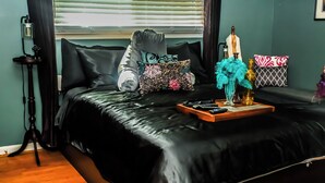 A bed with a black bedspread, a bedside table with a lamp, and decorative pillows. - Adults Only - Cozy, Kinky Hideaway Perfect for Couples (Atlanta)