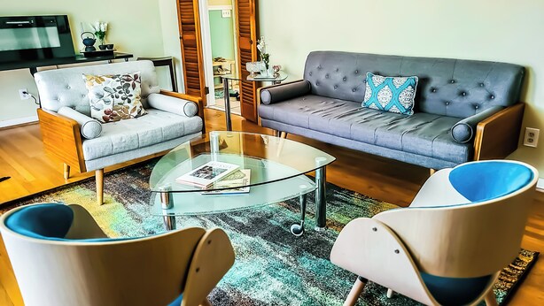 A living room with a sofa, two armchairs, a glass coffee table, and a television. - Adults Only - Cozy, Kinky Hideaway Perfect for Couples (Atlanta)