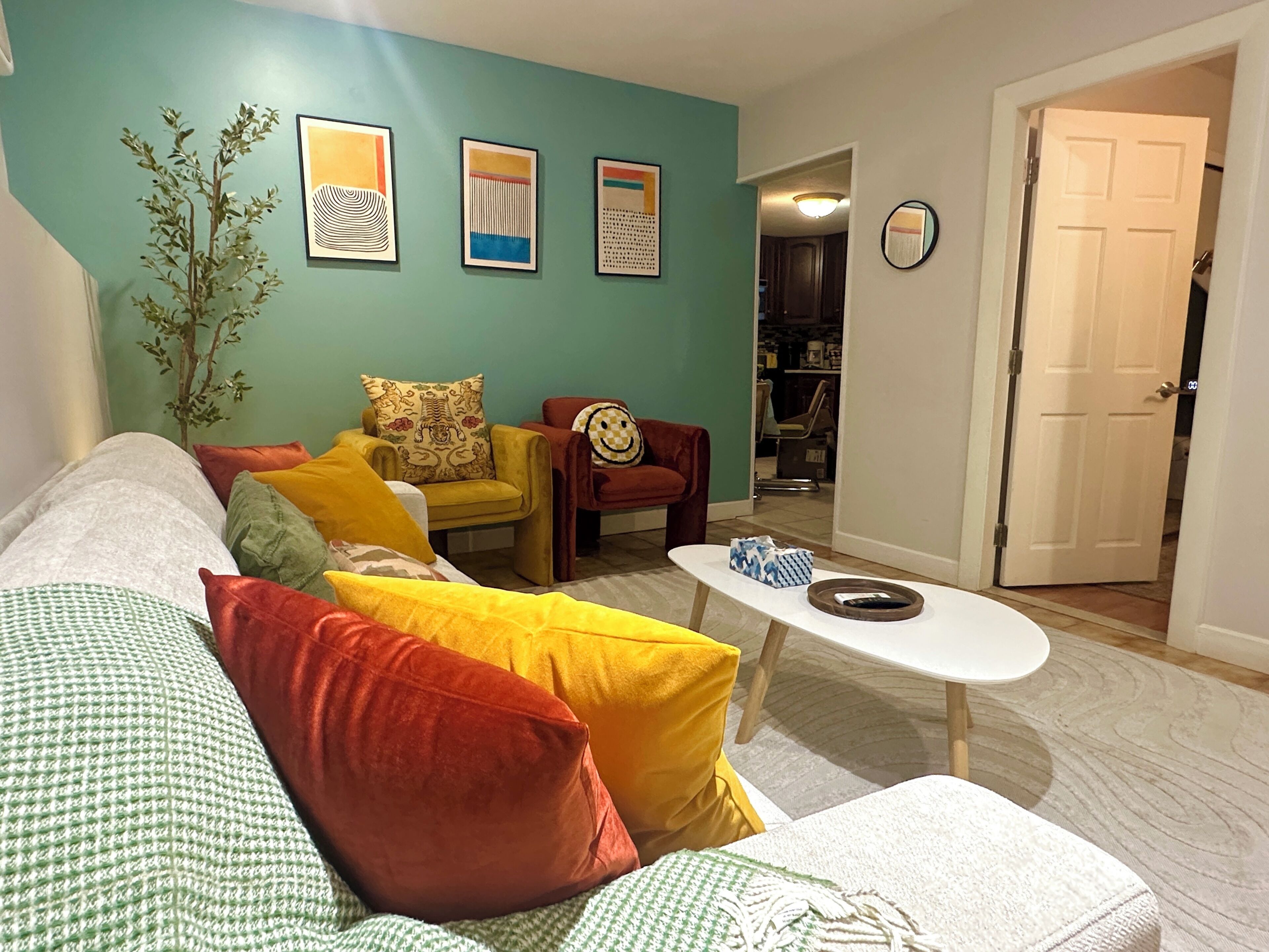 A living room with a sofa, armchairs, a coffee table, and a door leading to another room.