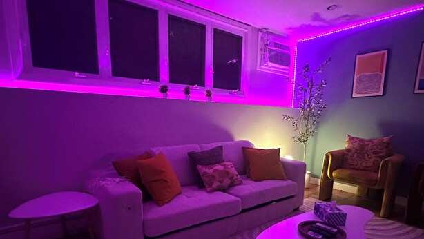 Ein modernes Wohnzimmer mit violetter Beleuchtung, ausgestattet mit einer Couch, einem Couchtisch und einem Sessel.