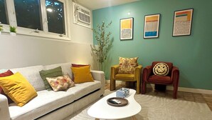 Ein Wohnzimmer mit einem weißen Sofa, einem kleinen weißen Couchtisch, einem roten Sessel und einer grünen Wand mit drei gerahmten Kunstwerken.