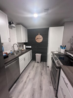 A modern kitchen with white cabinets, a black countertop, a stainless steel sink, and a black stove.