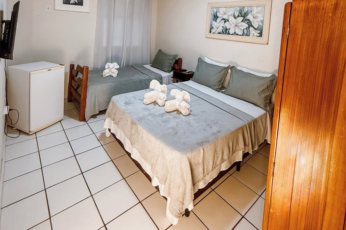 Ein Hotelzimmer mit zwei Betten, einem kleinen Kühlschrank, einem Fernseher und einem Bild an der Wand.