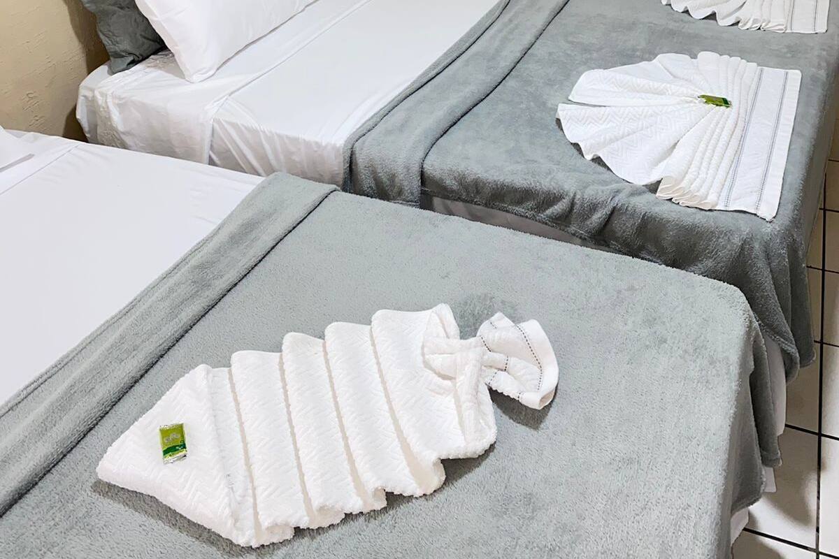 Ein Hotelzimmer mit zwei Betten, jeweils mit grauer Bettwäsche und weißen Kissen. Handtücher sind ordentlich auf den Betten drapiert.