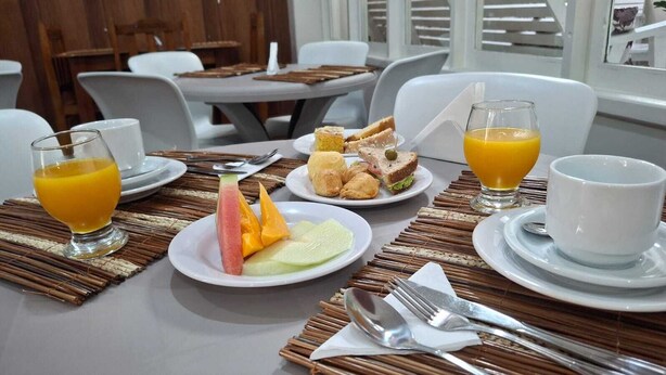 A breakfast setting with plates of fruit, sandwiches, and juice glasses on a table with a bamboo placemat. - Pousada da Orla  (Itacaré)
