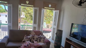 A living room with a sofa, a TV, and a window with an open door. - Pousada da Orla  (Itacaré)