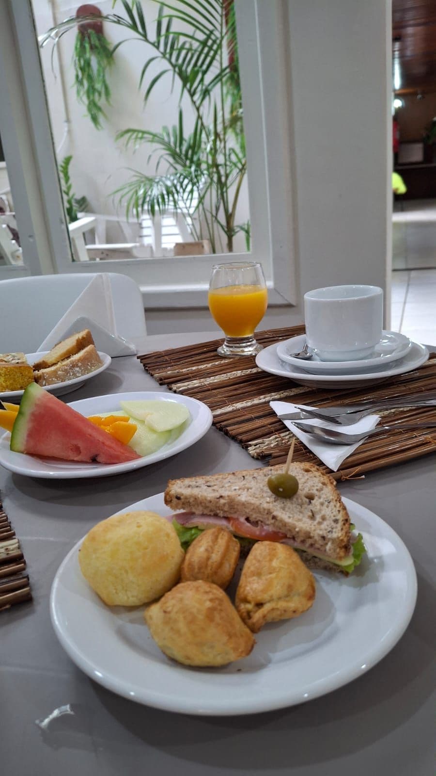 A breakfast setting with a plate of croissants, a sandwich with a green olive, and a glass of orange juice.