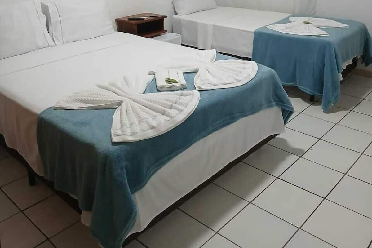 Ein Hotelzimmer mit zwei Betten, jeweils mit einer blau-weißen Tagesdecke, und einem kleinen Nachttisch.