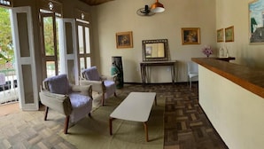 A room with a wooden floor, a white table, two armchairs, a mirror, and a wooden counter. - Pousada da Orla  (Itacaré)