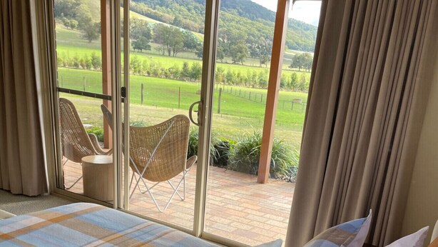Ein Schlafzimmer mit einem großen Bett, Blick auf einen Garten und einem Balkon mit Korbstühlen.