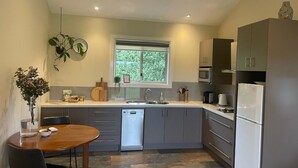 A modern kitchen with grey cabinets, a dishwasher, a microwave, and a refrigerator. There is a window above the sink, and a plant hangs on the wall. - Vista 2 drop the bags and look at the view (Yarra Junction)